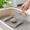 A hand is using a stainless steel cat litter scoop with a wooden handle and fine mesh sifter to scoop litter from a container