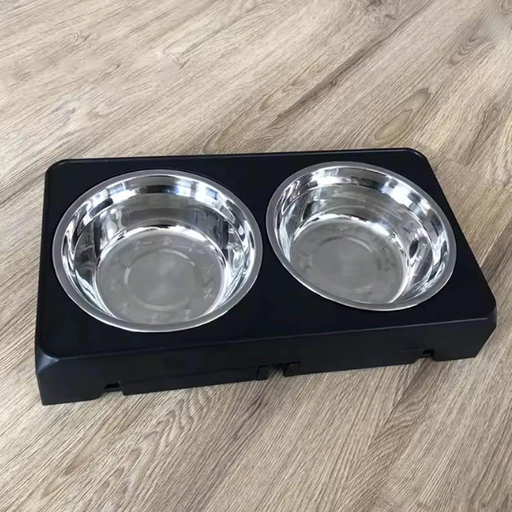 A black adjustable raised dog feeder with two stainless steel bowls resting on a light wood surface.