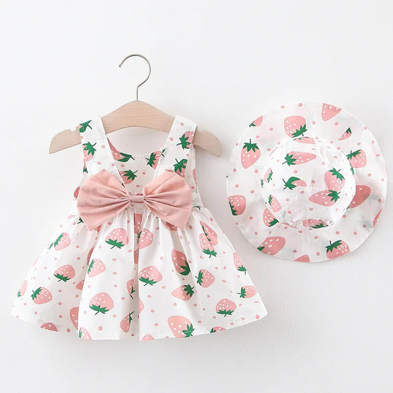 Rosa und weißes Erdbeermuster-Sommerkleid mit passender Mütze auf Holzständer.