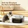 A gray and white cat sits next to a modern, black pet water fountain on a white mat.
