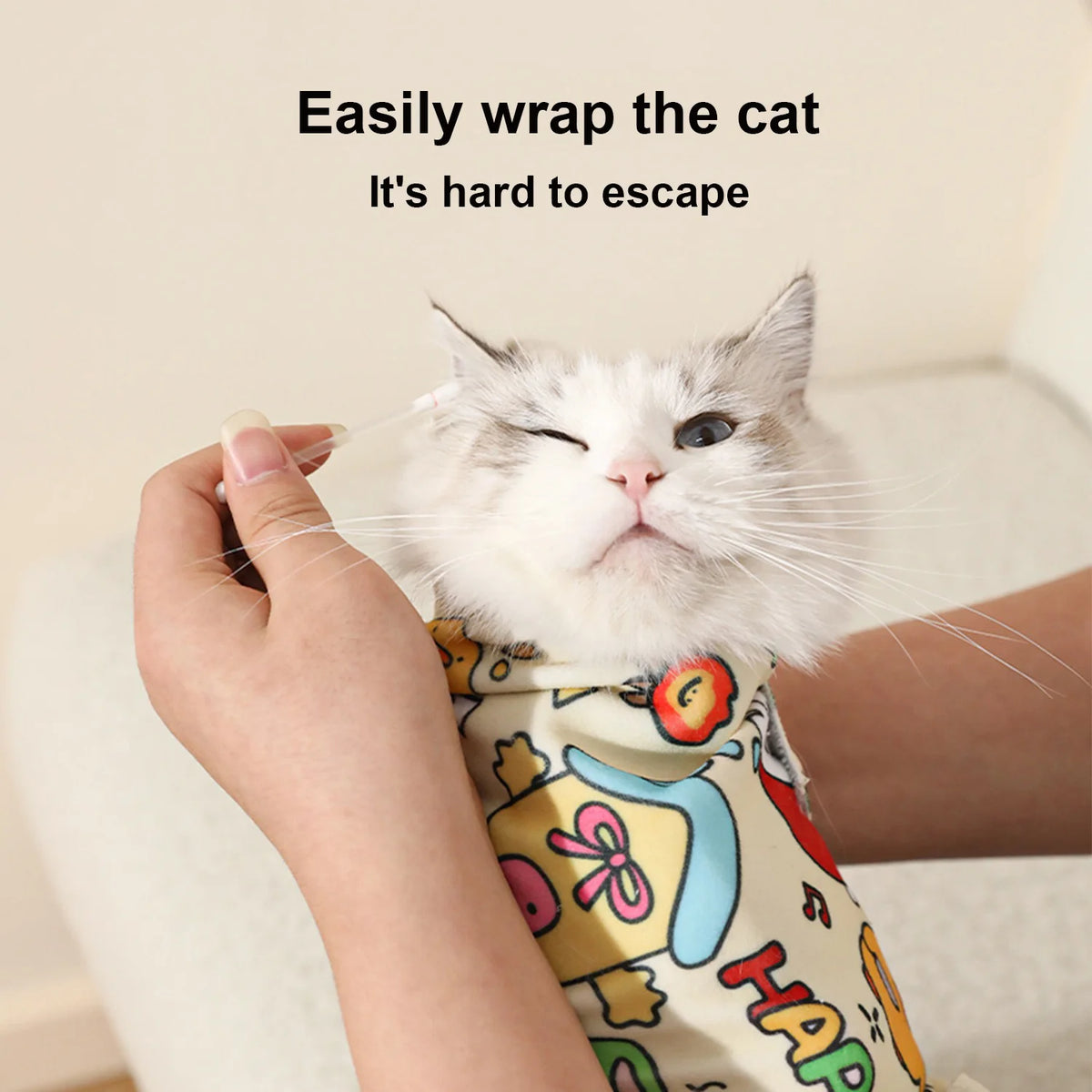 A white cat is being easily wrapped in a fabric swaddle for restraint.