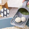 A gray reusable pet litter scoop is shown with a small white waste bag and loose litter on a beige surface.