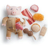 A plush pig toy dressed in a brown jacket with pink accents, surrounded by various pink and orange chew toys.