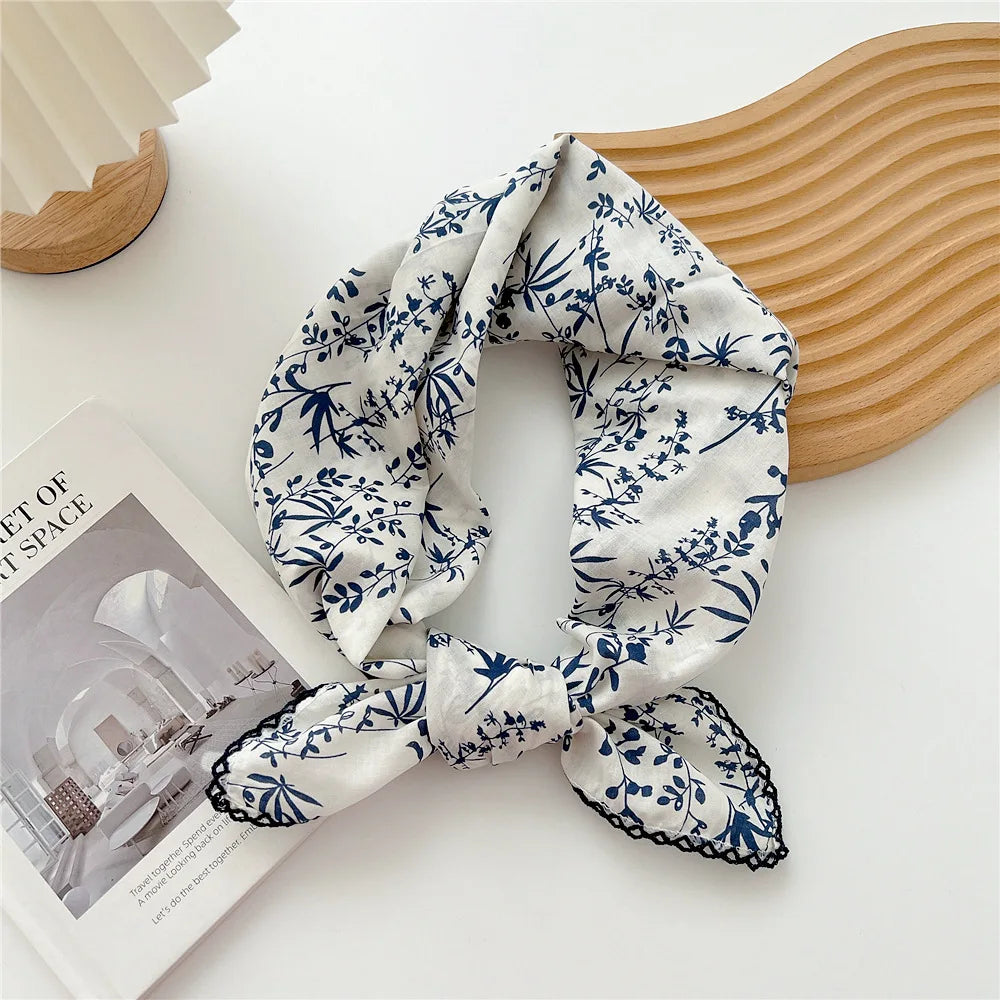 Écharpe en coton à motif floral blanc et bleu nouée, posée sur une surface en bois clair.