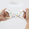 A pair of hands is holding a white, braided chew toy with colorful dots in an intertwined shape.