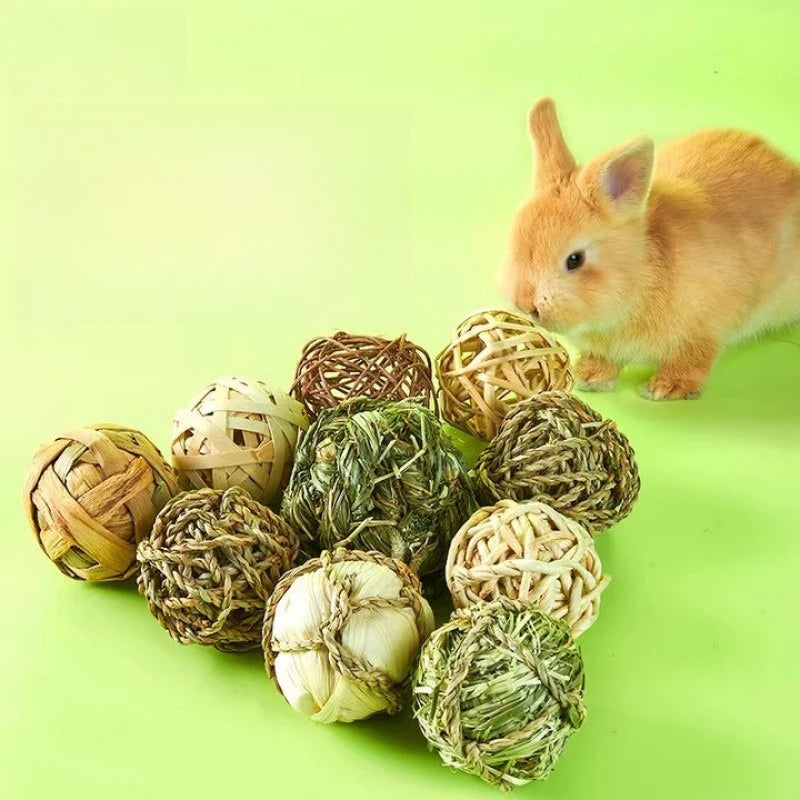A small orange rabbit sits next to several natural grass chew balls for small pets on a light green background.
