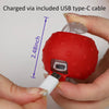 A red, spherical motion-activated cat toy ball is shown being held by a hand, with a USB type-C cable connected to it.