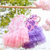 Vestidos de encaje de gasa rosa y morado para perros y gatos colgados en una barra de madera.