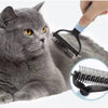 A hand is using a black stainless steel pet deshedding comb on a gray cat.
