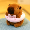 A brown capybara plush doll wearing a pink hoodie with wings, sitting on a blue surface.