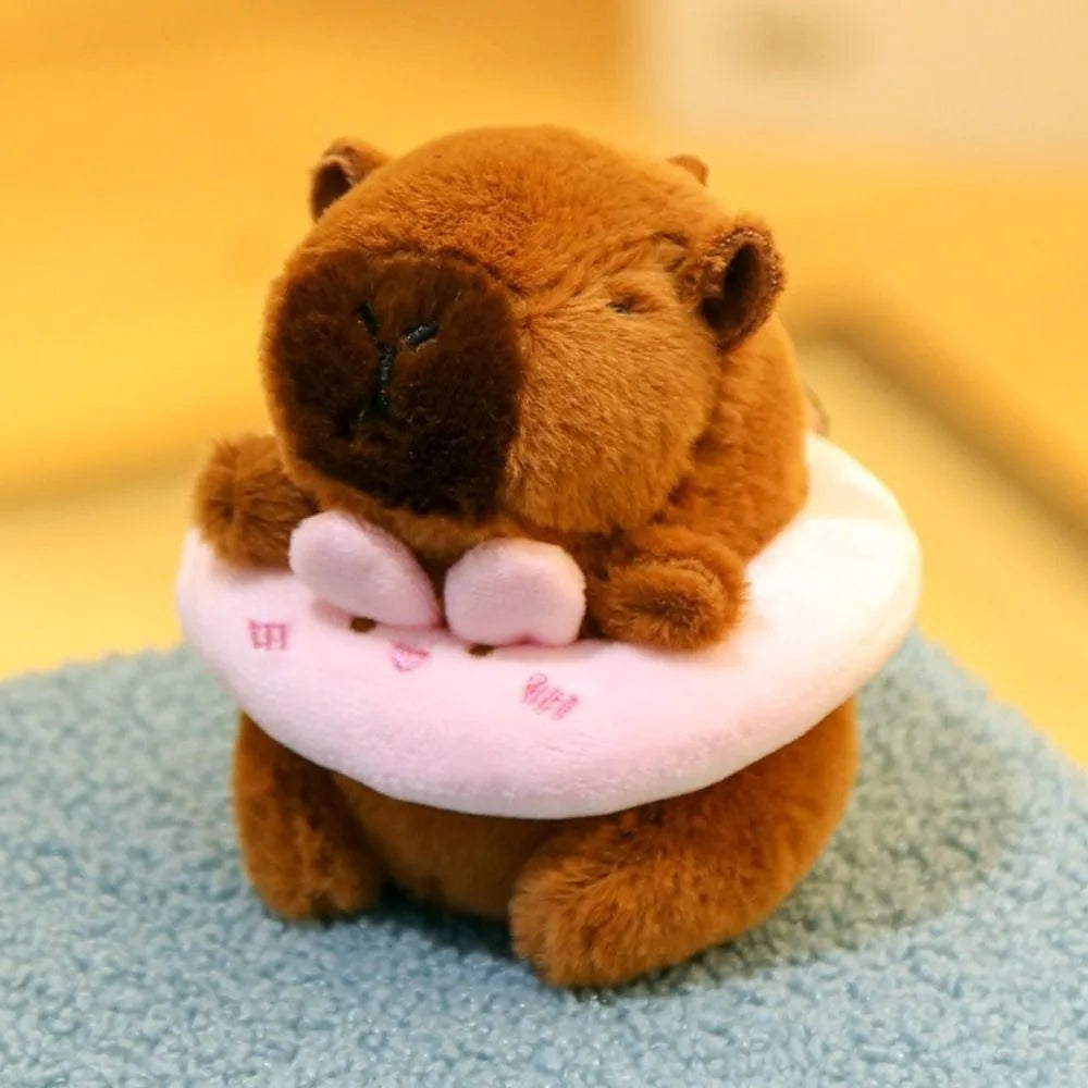 A brown capybara plush doll wearing a pink hoodie with wings, sitting on a blue surface.