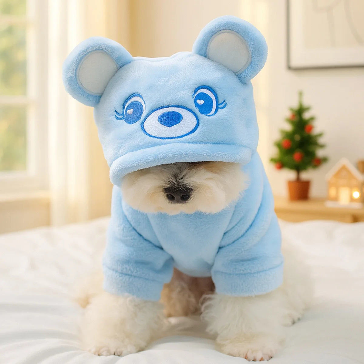 A light blue flannel hoodie for a small dog resembling a bear, sitting on white bedding.