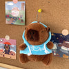 A brown capybara plush hoodie doll with light blue fabric and white trim is displayed on a cork board.