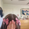 A hand is holding red plaid fabric bow hair clips on a person's dark brown hair.