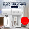 A white electric nano spray gun device with a clear bottle and charging port is shown on a table.