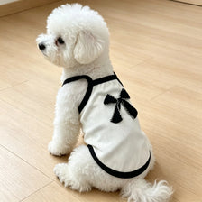 A white ribbed pet vest with a black bow knot for a small dog lying on a wooden floor.