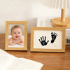 A wooden photo frame displays a baby's face and a pet paw print, used as a keepsake kit.