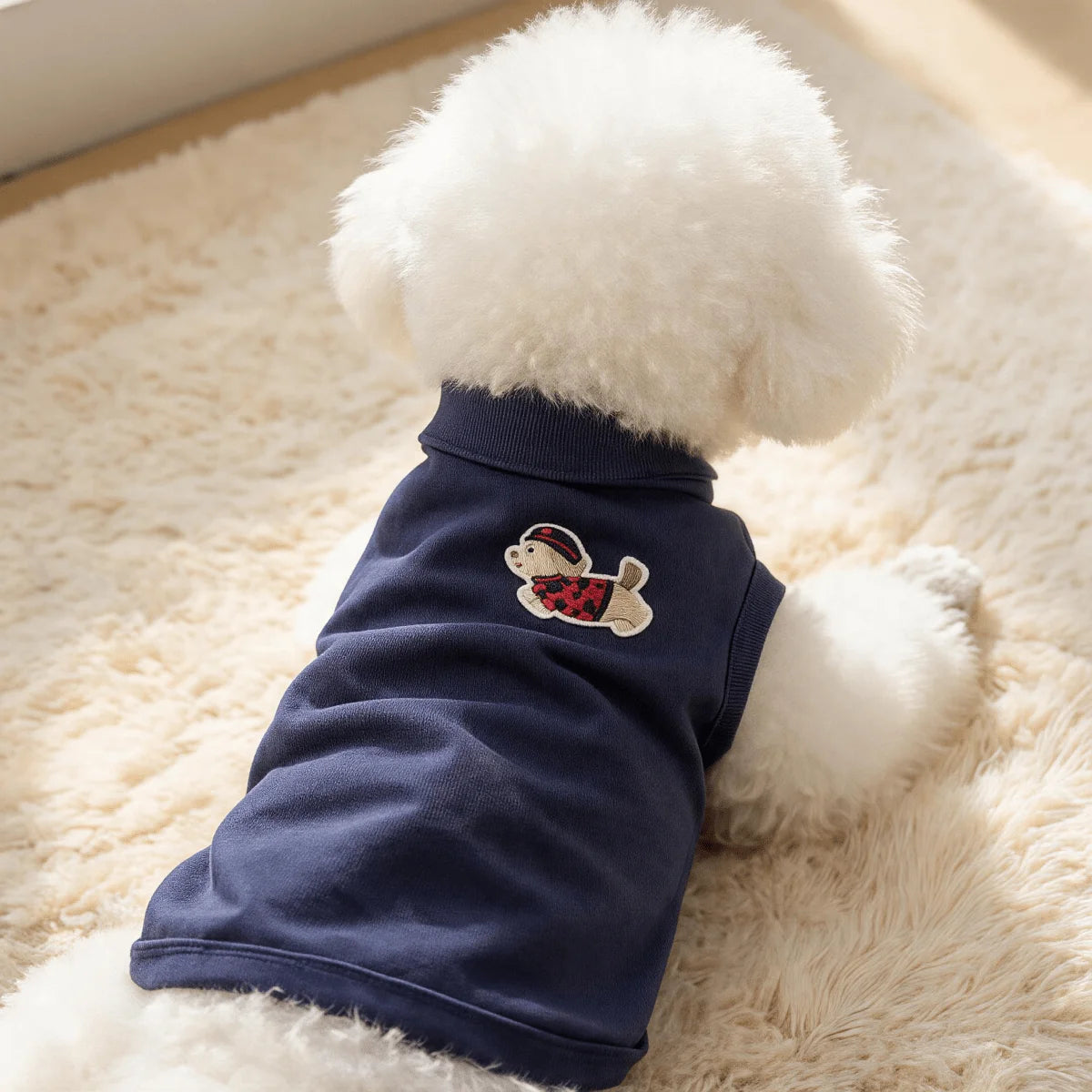 A navy blue sleeveless vest for a pet with white fluffy fur, featuring a cartoon embroidery.