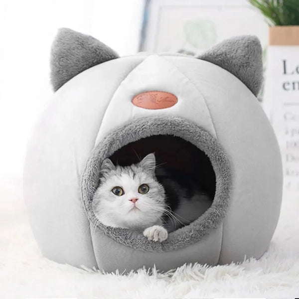 A gray plush cat cave bed with large ears and an entrance, resting on white fur.