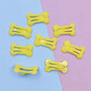 Yellow bone-shaped hair clips arranged on a light blue and pink background.