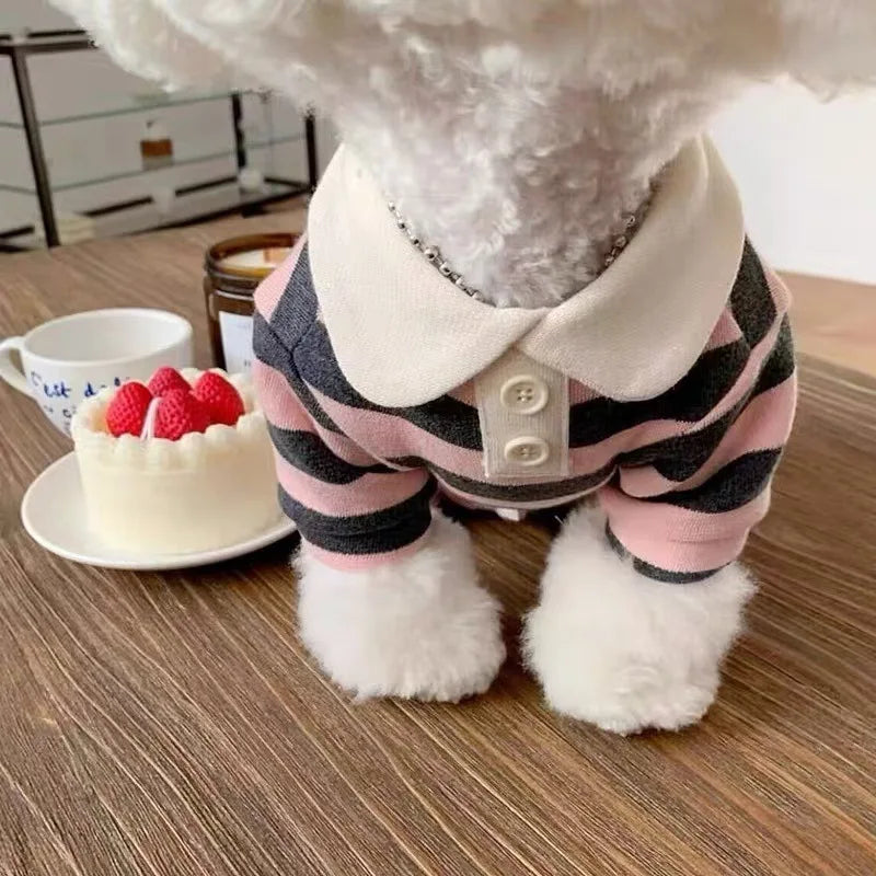 A fluffy white dog hoodie with a pink and black striped collar and paws sitting on a wooden surface.