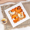 A white plate features ten orange and yellow window cakes with secure bases arranged on a rustic cloth.