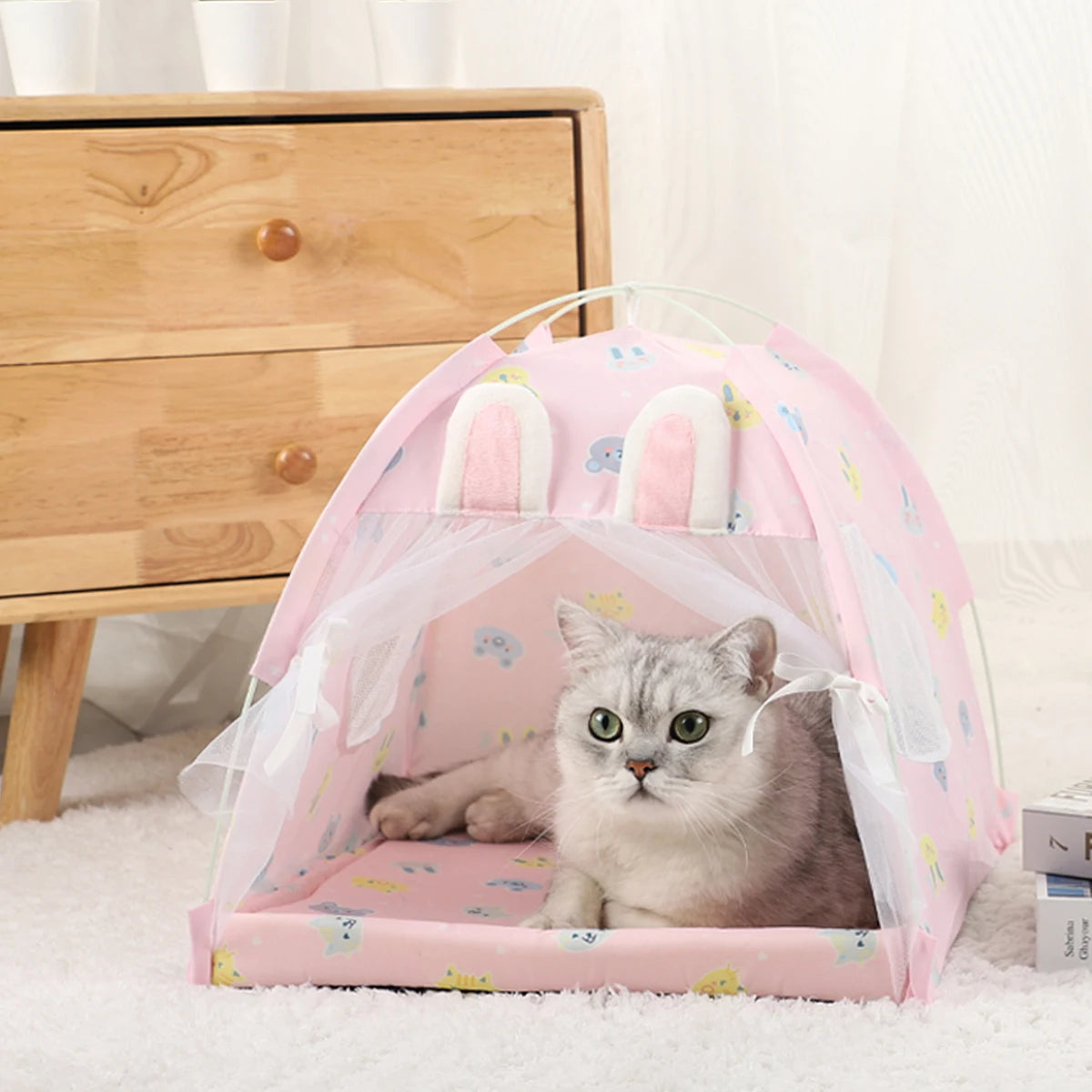 A gray cat is resting inside a pink mesh tent bed for cats on a white carpet.