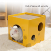 A yellow cardboard cat scratching house with a textured entrance and several circular holes, placed on a white fluffy surface