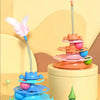 A colorful interactive cat turntable toy with a feather wand and rolling balls displayed on a light yellow surface.