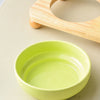 A bright lime green ceramic pet bowl is shown on a light surface, with a wooden stand partially visible.