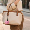 A beige reusable pet hair roller bag carried by a person, featuring a pink cartoon-shaped charm.