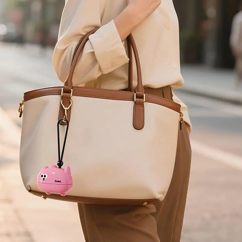 A beige reusable pet hair roller bag carried by a person, featuring a pink cartoon-shaped charm.