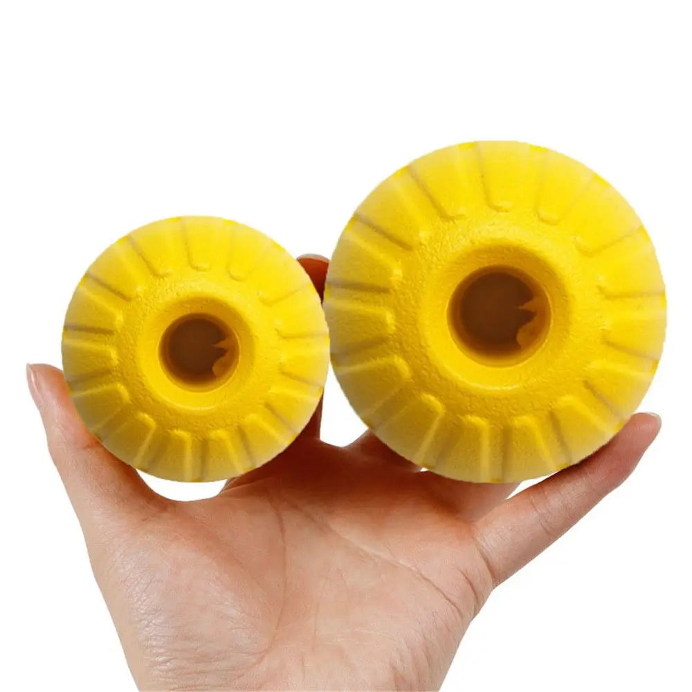 A hand holds two yellow rubber fetch balls with textured surfaces.