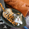 A tabby cat wearing an orange and black striped fleece jumpsuit is resting in a green fabric bowl.