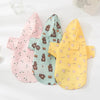 Three patterned dog raincoats in pink, teal, and yellow laid out on a white surface.