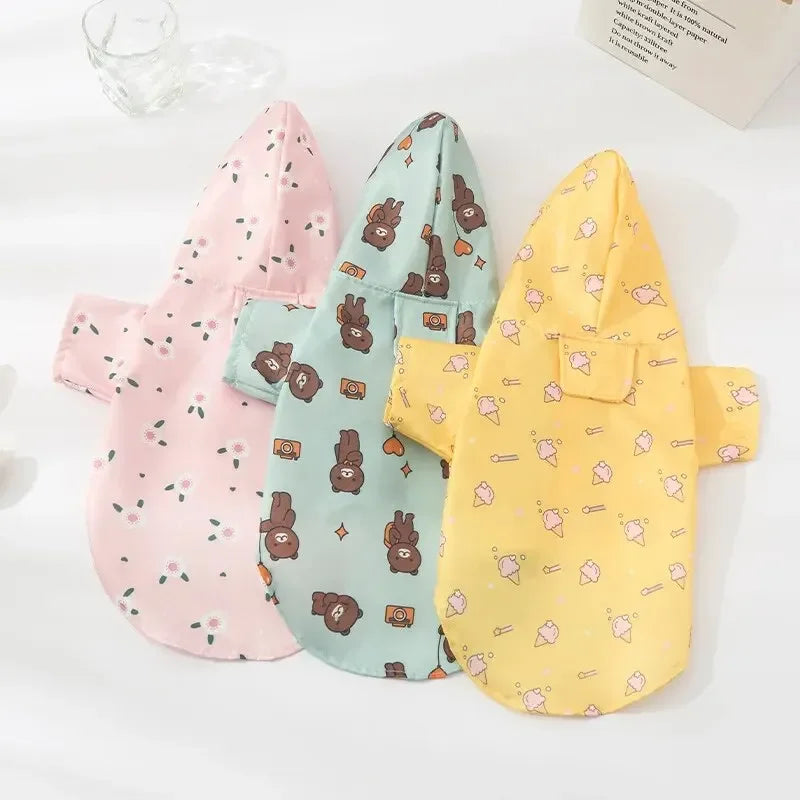 Three patterned dog raincoats in pink, teal, and yellow laid out on a white surface.