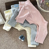 A collection of soft stretch dog pajamas in various colors including pink, gray, and cream, laid out on a brown carpet.