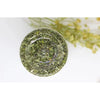 A round, translucent green glass dish filled with dried natural catnip and mint grass for feline relaxation.