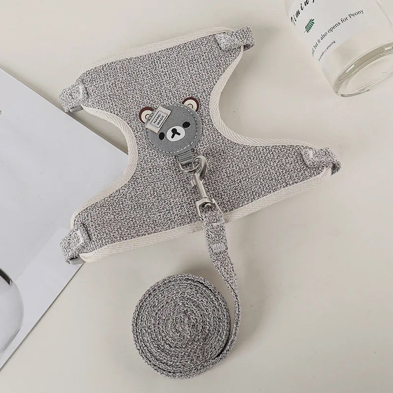 A gray padded rabbit harness and leash set with a round tag and coiled leash is shown on a white surface.