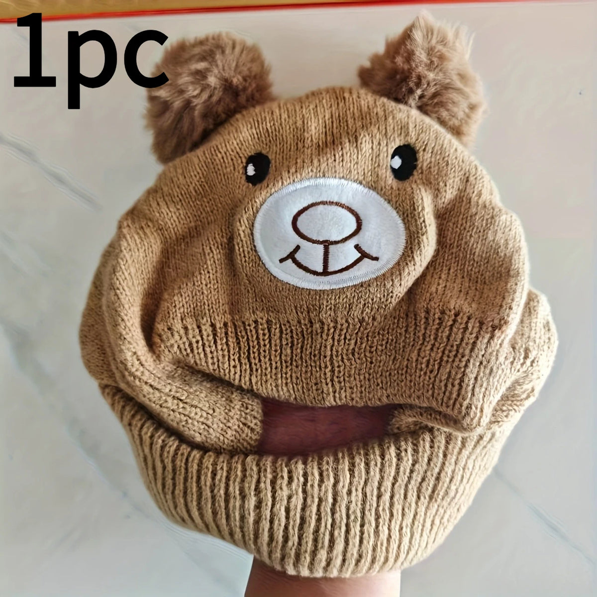 A knitted beige bear hat and scarf set featuring bear ears and a circular embroidered face.