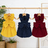A display of three vintage corduroy pet dresses in yellow, navy blue, and burgundy hanging on a wooden rack.
