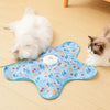 A light blue silicone cat teaser toy with colorful feathers is placed on a wooden floor next to two cats.