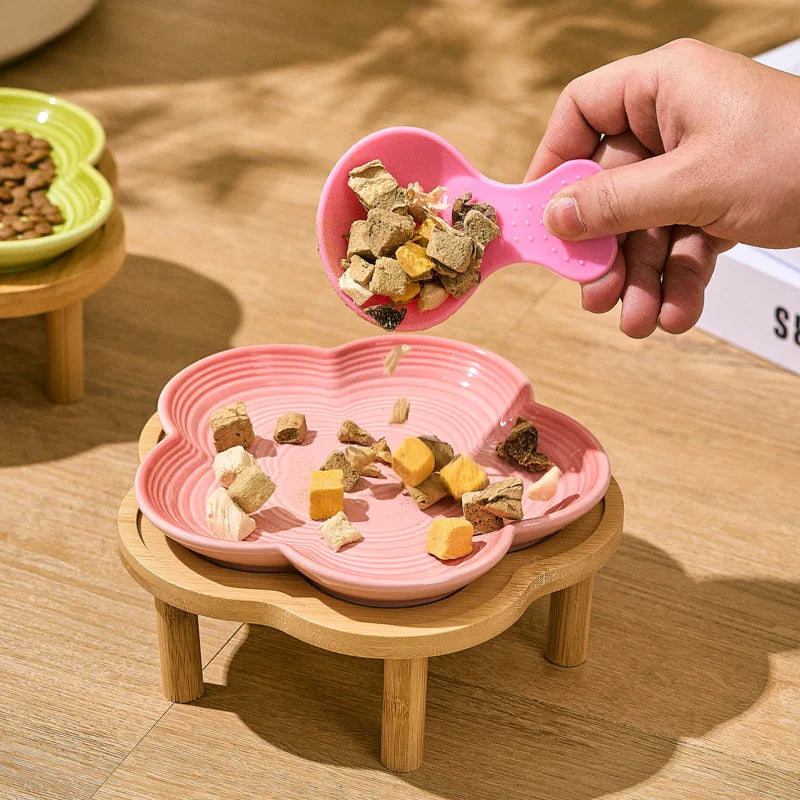 Une main tient un bol à animaux en céramique rose avec de la nourriture, positionné au-dessus d'un bol assorti rose sur un su
