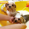 A dog is being bathed with foam dispensed by an orange electric device in a yellow bowl.