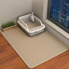 A large honeycomb cat litter mat is placed on a wooden floor next to a window with a city view.