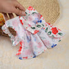 Robe d'été pour chien rose et blanc à motifs floraux avec un nœud en dentelle tenue par une main.