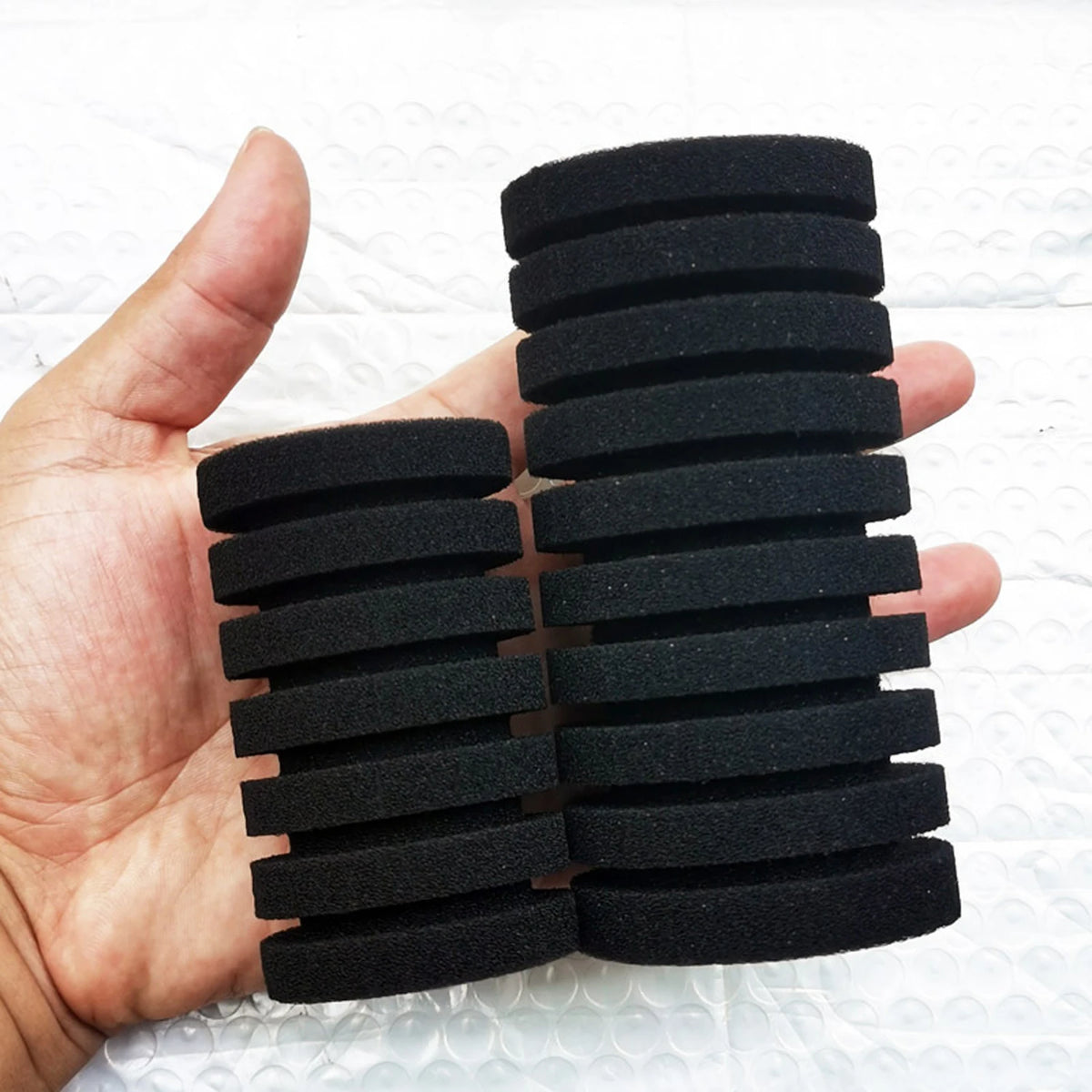 A hand holds a stack of black biological aquarium sponge filter discs.