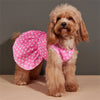 A light brown poodle wearing a pink polka dot dog dress with a ruffled skirt.