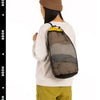 A person wearing a beige sweater and olive pants is holding an open mesh storage bag with a drawstring closure.