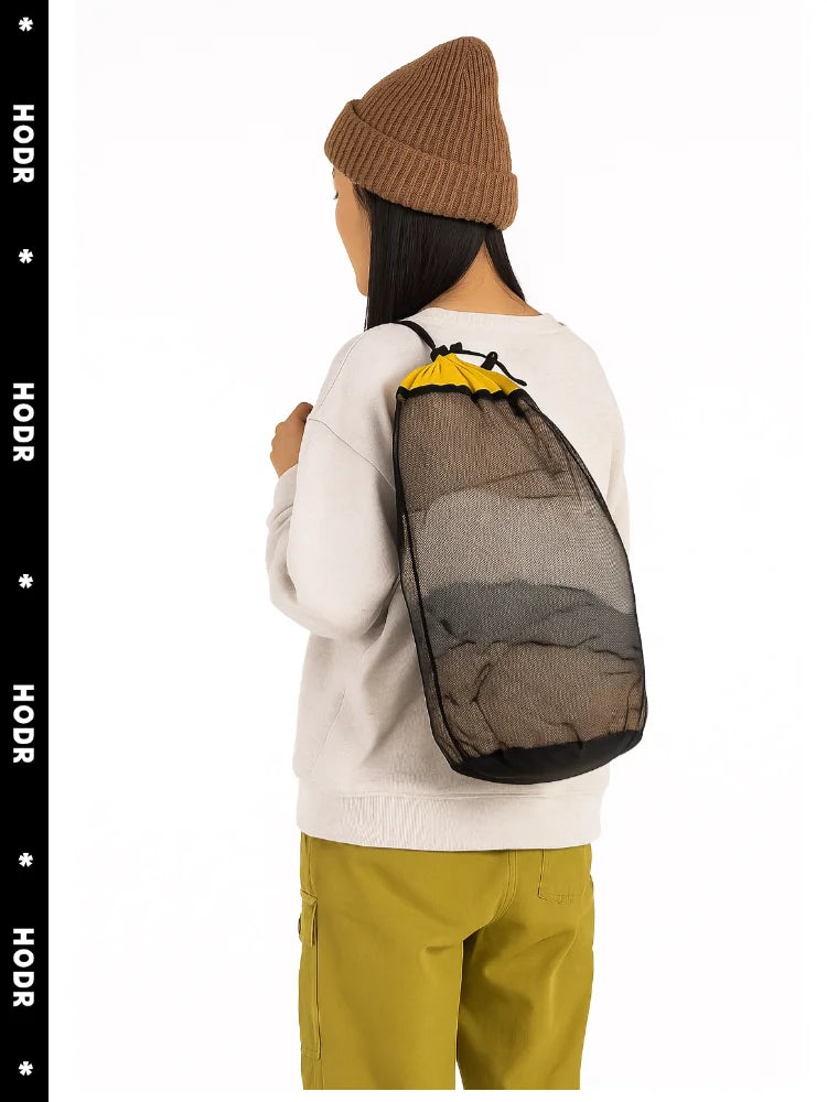 A person wearing a beige sweater and olive pants is holding an open mesh storage bag with a drawstring closure.